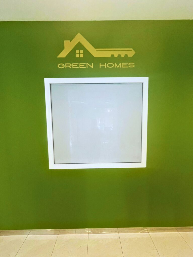 Pared interior verde con logotipo de Green Homes y ventana enmarcada